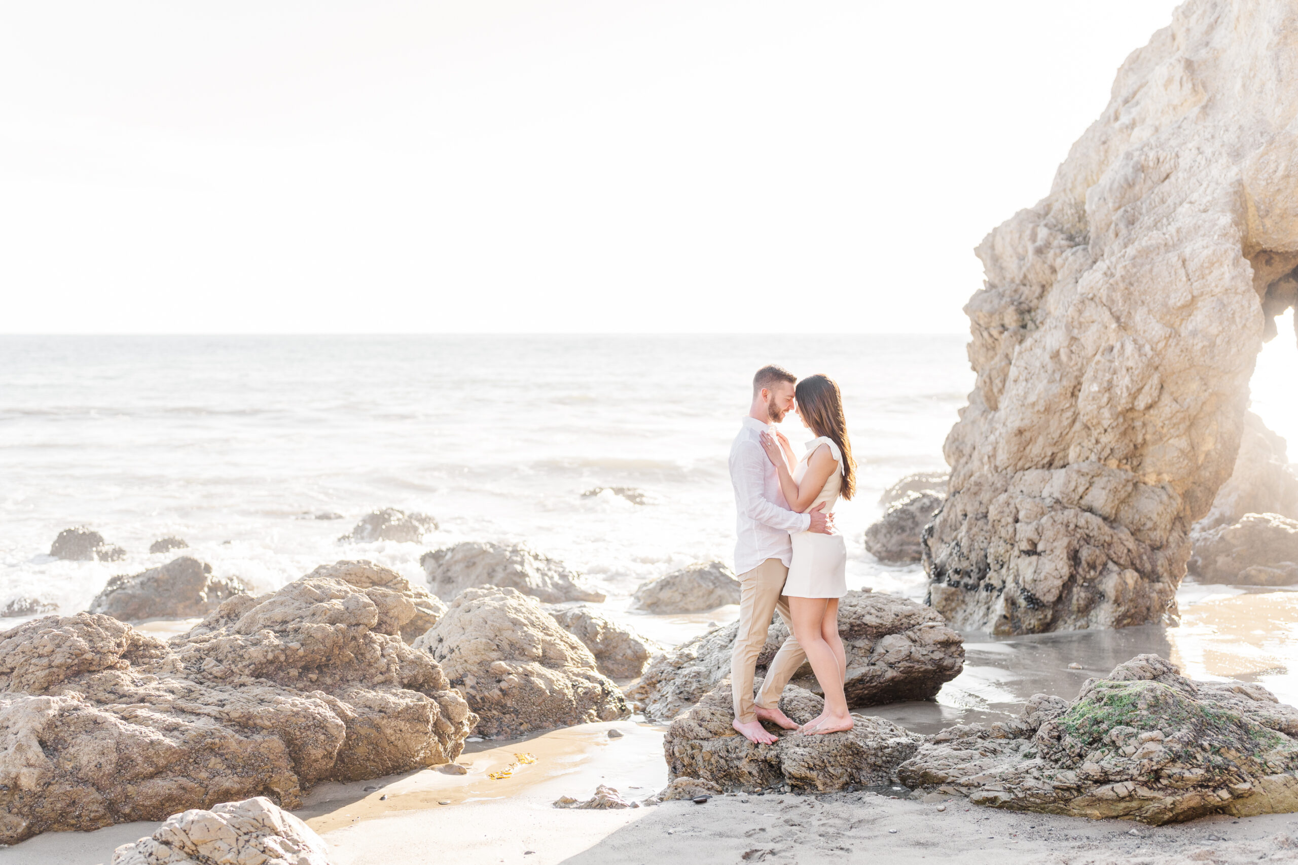Couple stands on a rock forehead to forehead on Malibu beach during sunset